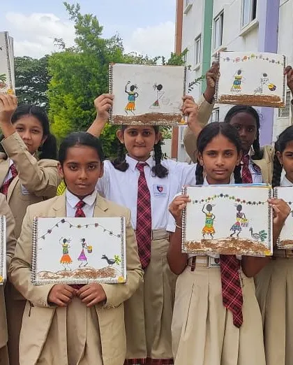 A group of girls proudly holds up their mud art creations, showcasing their hard work and creativity.