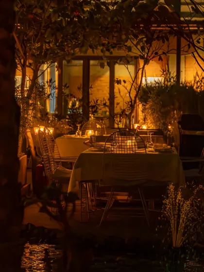 A wide shot of an outdoor dining area at night, with tables aglow with candlelight. This photo establishes the restaurant's beautiful and serene atmosphere.