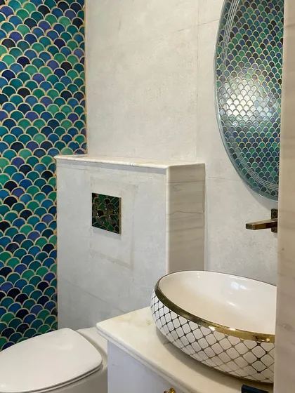 Bathroom details are crucial for a cohesive design. In this powder room, we used playful fish-scale tiles in shades of blue and green, paired with gold-accented fixtures to create a small but luxurious space.