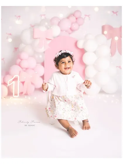 A radiant smile for her first birthday. The soft pink and white bow theme creates a delicate and beautiful backdrop for her special day.