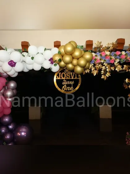 The entrance to an elegant floral-themed party. The decor includes a balloon and flower arch over a wooden pergola, with a personalized gold sign welcoming guests.