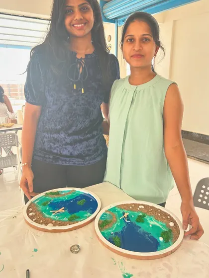 Two participants proudly display their finished beach-themed resin art pieces.