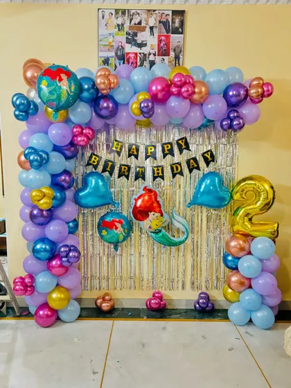 A mermaid-themed second birthday party with a colorful balloon arch against a silver tinsel backdrop.