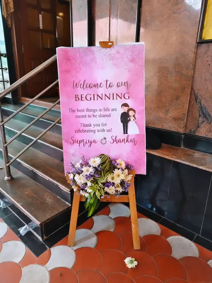 A charming welcome board with a pink watercolor design and a cute caricature of the couple, adding a personal touch to the event entrance.