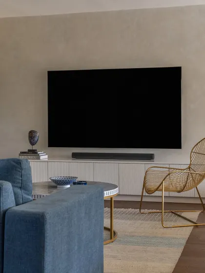 The media wall in the family lounge features lime-washed walls for a soft, textural effect. The gold wireframe chair adds a sculptural element to the cozy and contemporary space.