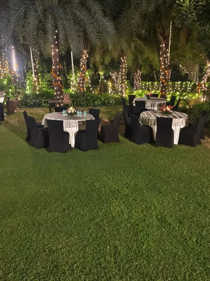 A wide view of the lawn seating for a Diwali party, showing the ambient lighting from the fairy lights on the trees.