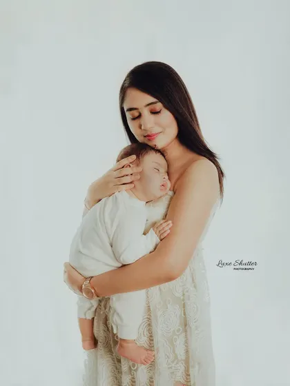 A mother holding her sleeping baby close to her heart. The simplicity of the pose and the white outfits create a timeless and peaceful image.
