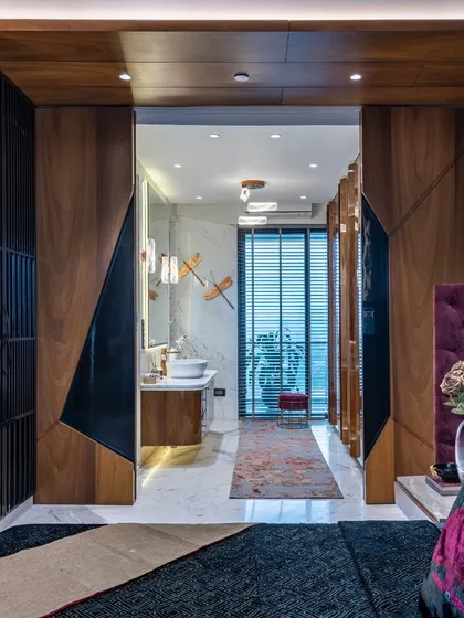 A view from the master bedroom into the ensuite bathroom. The design features dramatic, geometric wooden doors that slide open to reveal a bright, modern bathroom, creating a seamless transition between the two spaces.
