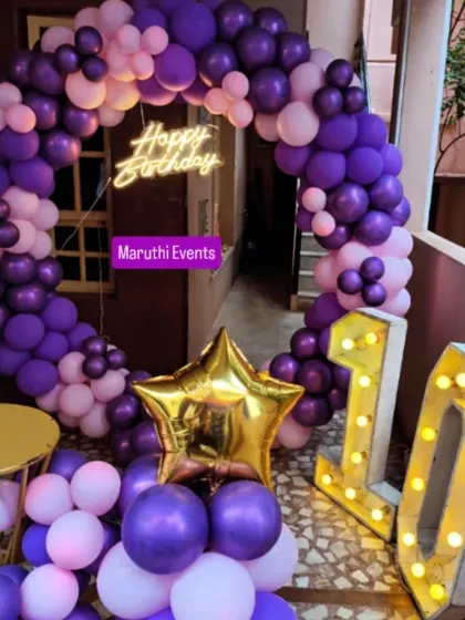 A 10th birthday party with a purple and pink circular balloon arch. The setup includes a neon sign and large, light-up marquee numbers.