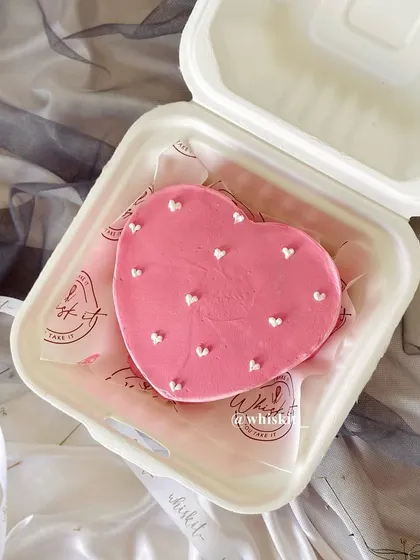 A sweet, heart-shaped bento cake in pink with tiny white hearts. It's an adorable mini cake for an anniversary or just to say "I love you."