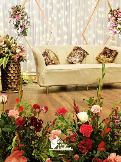 A close-up of the reception stage decor, showing the elegant sofa with sequined cushions and the lush floor arrangements of red and pink flowers that framed the seating area.