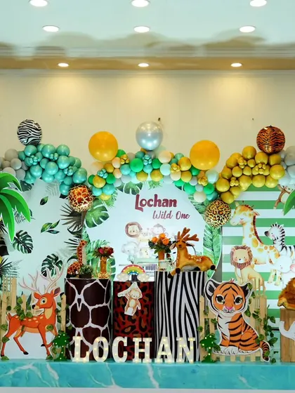 A vibrant 'Wild One' jungle safari theme for Lochan's first birthday. The stage is filled with animal print pedestals, cute animal cutouts like tigers and zebras, and a lush balloon garland.