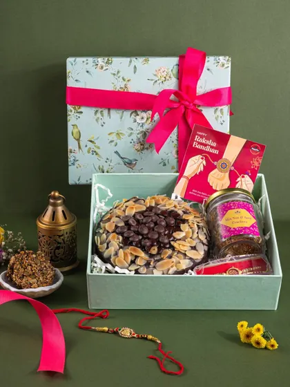 A beautifully packaged Rakhi hamper featuring a large almond-chip cake, styled with a rakhi and a traditional lantern.