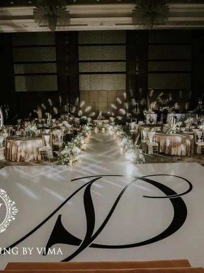 A classic and elegant reception setup symbolizing everlasting love. The stage features a modern, minimalist backdrop with custom monograms, floral arrangements, and soft lighting.