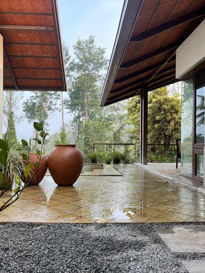 A view of the wet, stone-paved patio after a rain shower, looking out towards the misty forest. The large terracotta urns are a nod to traditional local crafts.