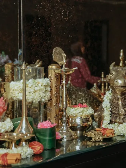 A reflection of the decorated puja table, showing the layers of flowers, brass idols, and lamps. The mirror adds depth and elegance to the traditional setup.