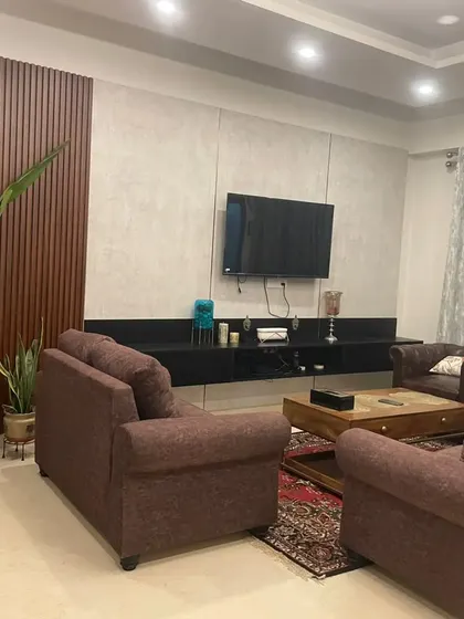 A delivered project showcasing a comfortable living room with dark brown sofas and a minimalist black TV console. The wood-paneled accent wall adds warmth and texture to the space.