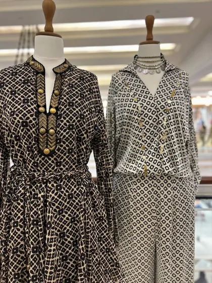A closer look at two of the black and white outfits, one a belted dress with gold button details and the other a stylish wrap-style jumpsuit.