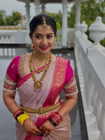 This image showcases the harmony between the bride's makeup, her vibrant pink saree, and her traditional gold temple jewellery. The look is both classic and full of life.