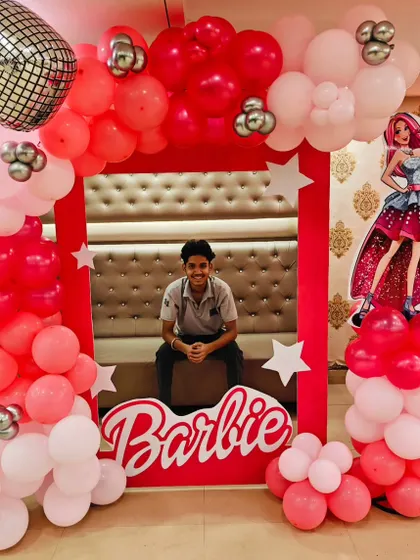 A fun Barbie-themed photo booth for a birthday party. The frame is made of pink and red balloons, with a disco ball accent and the classic Barbie logo.