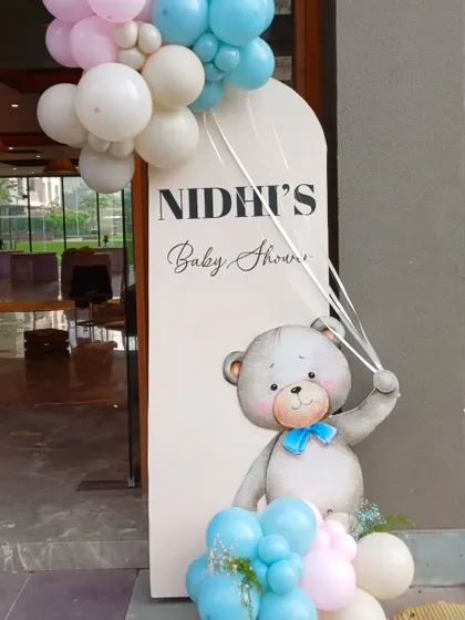 A dreamy welcome sign for a baby shower. The teddy bear theme is carried through with a cute illustration and a pastel balloon garland.