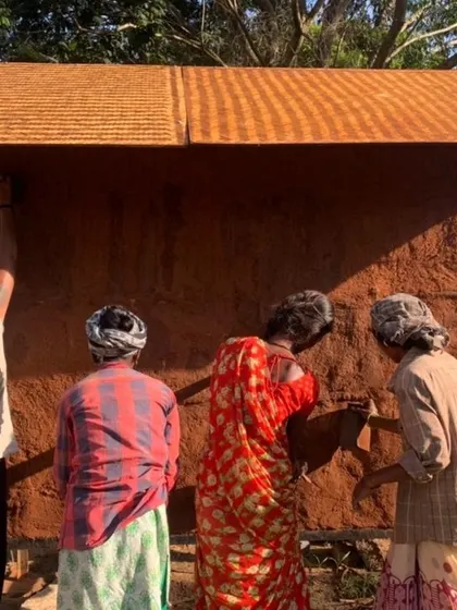 A team of women applying the final plaster coat to an earthen wall. This shows the finishing stages of a natural building project, where attention to detail is key.