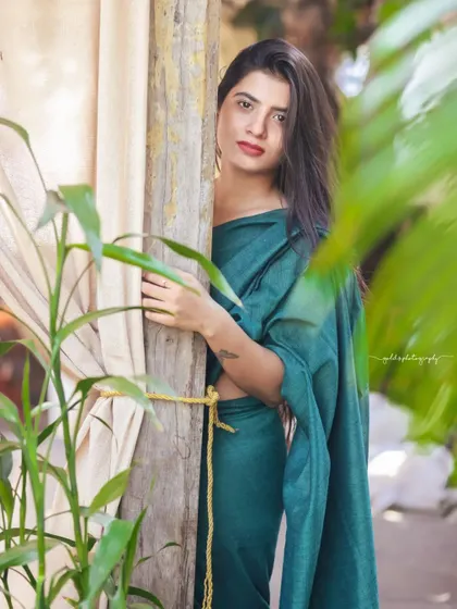 A modern take on saree styling. The model wears a teal saree paired with a contemporary black top, shot in a cafe with earthy tones. This shows how traditional wear can be styled for a modern, chic look.