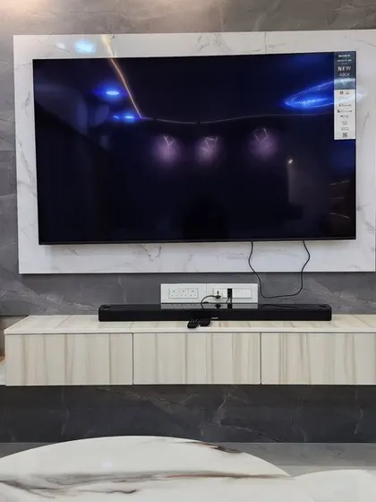 A close-up of the TV unit from a finished site, featuring a large-format tile background, wood-finish fluting, and a floating console.