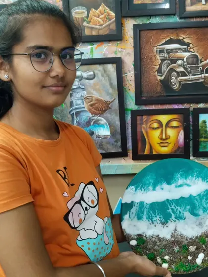 A student holding her beautiful resin art piece depicting a beach scene. Learn to create realistic waves and textures using resin, sand, and shells in our specialized workshops.