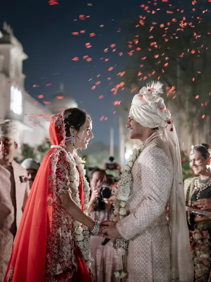 Anaaya and Nikunj share a moment during their varmala ceremony, surrounded by falling petals and the happy faces of their loved ones. The evening light adds a magical glow to their connection.