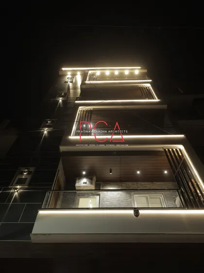 A powerful low-angle night shot of The Cursive Abode, where the facade lighting appears to carve the building out of the darkness.