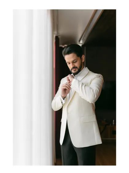 A groom adjusts his cufflinks by a window. This classic, candid shot captures a moment of final preparation and quiet anticipation.