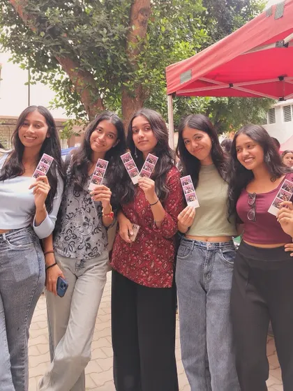 A group of friends enjoying the outdoor setup at a college fest, photo strips in hand.
