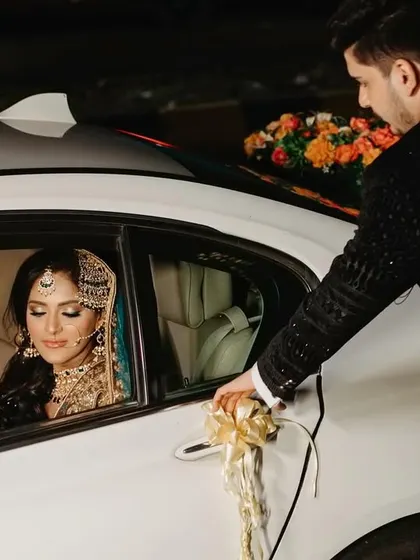 The groom's chivalrous gesture of opening the car door for his bride. This cinematic shot captures a moment of care and elegance as they arrive at their reception.