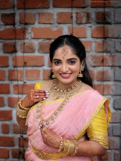 A stunning bridal portrait against a simple brick wall. The contrast makes her beautiful pink and yellow saree and intricate jewelry pop.