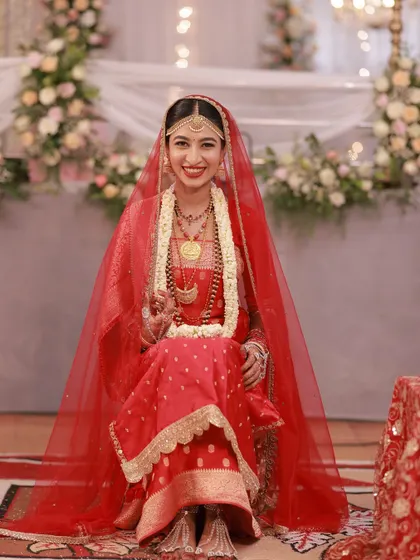 The bride on her wedding day, looking radiant in her red saree and veil. Her makeup is classic and bold.