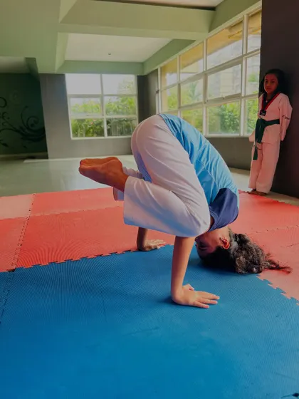 A student holds a challenging arm balance pose (Bakasana or Crow Pose), showing the strength and balance gained from our training.