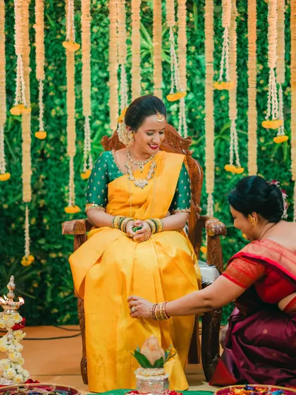 A mother blesses the bride during a traditional pre-wedding ceremony, set against a backdrop of fresh flowers and greenery.