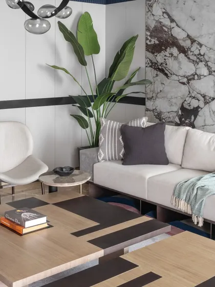 A detailed view of the living room's styling, featuring a geometric coffee table, plush cushions, and a large plant against a marble backdrop. Every detail is curated to enhance the room's modern and luxurious feel.
