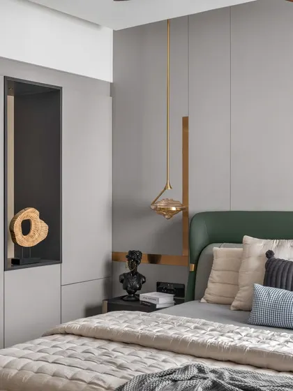 A close-up of a bedroom corner, showcasing the details. A deep green headboard is paired with grey wall paneling and gold accents. The sculptural pendant light and curated objects in the display niche reflect a sophisticated, art-forward approach to design.