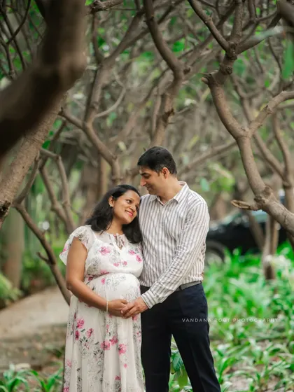 A lovely portrait of an expecting couple with their daughter, enjoying a family day out in a lush green park.