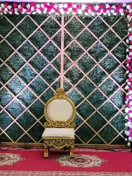 A stylish Mehandi backdrop with a green grass wall, a gold geometric lattice, and a border of pink and white flowers.