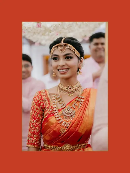 A close-up portrait of a smiling South Indian bride in her traditional wedding attire, framed in red, highlighting her intricate jewelry and happy expression.