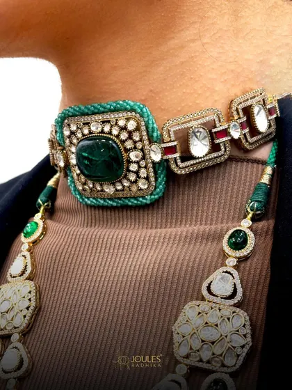 A closer look at the intricate details of a layered bridal set. The choker features a central emerald surrounded by polki diamonds, connected to a longer necklace with geometric and floral motifs.