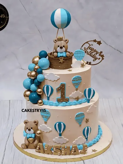 A sky-high teddy celebration for a first birthday. This 3kg black forest cake features a teddy in a hot air balloon, surrounded by blue and gold decorative balls and fondant clouds.