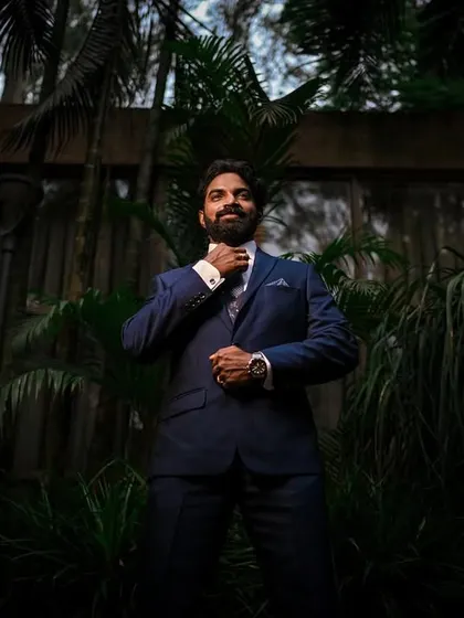 A stylish, low-angle shot of the groom adjusting his tie, surrounded by lush greenery at night.