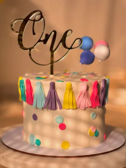 A festive and colorful cake for a first birthday party. This lemon-flavored cake is decorated with a fun tassel garland, confetti dots, and a balloon topper.