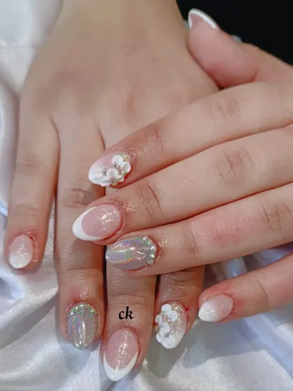A close-up of a nude bridal set with various textures, including a French ombré, holographic glitter, and 3D flowers with gold bead centers.