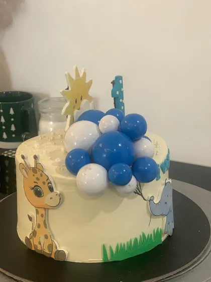 A jungle animal themed cake for a first birthday. This design features cute cartoon animals and a cascade of blue and white chocolate balls.