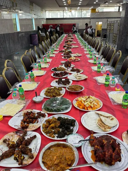 A complete Dastarkhwan setup ready for a wedding reception. The long table is laden with a variety of our best dishes, including multiple chicken starters, mutton curries, fruit salad, and fresh bread.